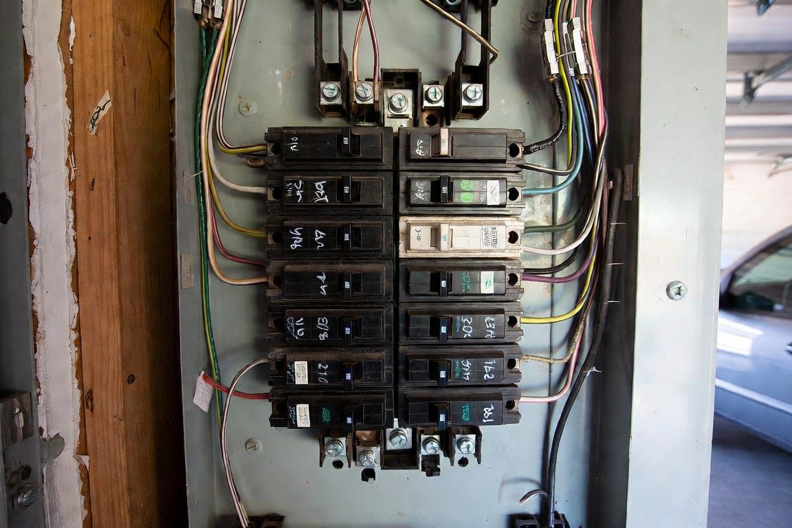 Close-up of an older residential breaker panel with nearly every breaker space filled, handwritten labels, and mixed wiring entering the box.